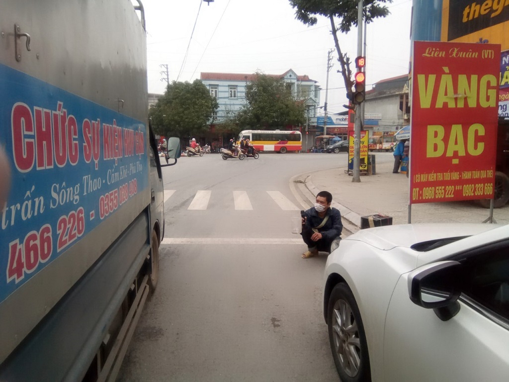 Một người ăn xin ngồi chắn đầu xe ôtô tại thị trấn Sông Thao, huyện Cẩm Khê (Phú Thọ)