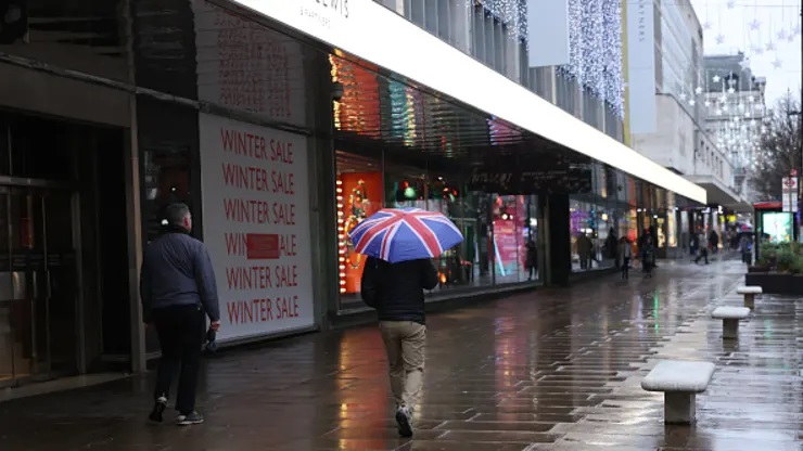 Một người đi bộ mang ô Union Jack đi ngang qua bảng hiệu bán đồ mùa đông bên ngoài cửa hàng John Lewis dọc đường Oxford ở London, Anh.