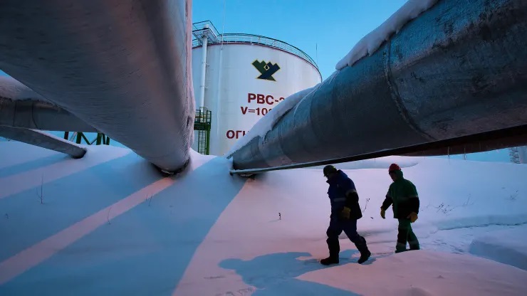 Các nhân viên đi qua bên dưới các đường ống dẫn đến các bể chứa dầu tại nhà máy chế biến dầu khí trung tâm tại các mỏ dầu của Công ty Phát triển Dầu khí Salym gần hệ thống đá phiến Bazhenov ở Salym, Nga.